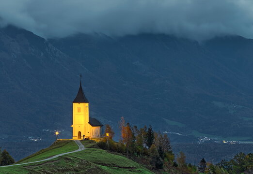 Lightened St.Primus and Felician hilltop Gothic church on a grassy ridge backed by the Karavanke range, on a cloudy autumn sunset. Jamnik-Slovenia-177