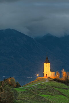 Lightened St.Primus and Felician hilltop Gothic church on a grassy ridge backed by the Karavanke range, on a cloudy autumn sunset. Jamnik-Slovenia-178