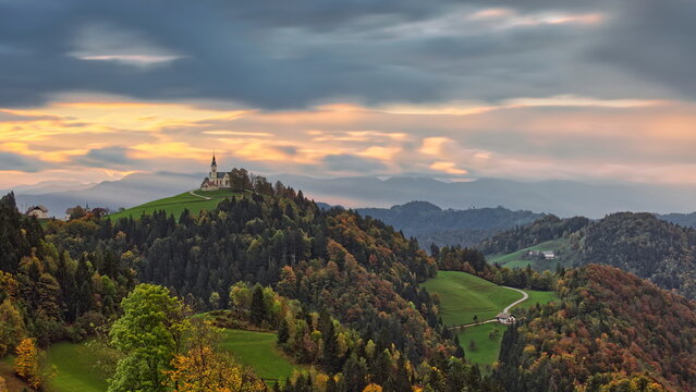 Hilltop St.Leonard parish church seen NW-to-SE in a colorful cloudy sunrise, in the pre-Alpine wooded hills of Polhov Gradec. Crni Vrh-Slovenia-183
