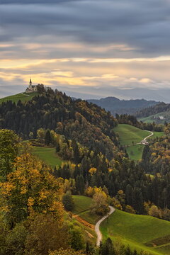 Hilltop St.Leonard parish church seen NW-to-SE in a colorful cloudy sunrise, in the pre-Alpine wooded hills of Polhov Gradec. Crni Vrh-Slovenia-184