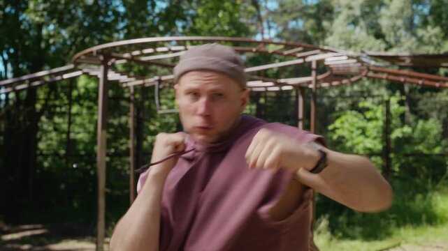 Portrait of Caucasian young adult man shadow boxing outdoors, throwing punches directly at camera. Footage is ideal for fitness app promotions, sports brand marketing, and motivational campaigns
