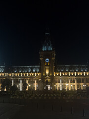 Naklejka premium City Hall glows at night, Bucharest. People stroll near the city hall as it lights up the night sky in Bucharest. The building stands tall against the dark.