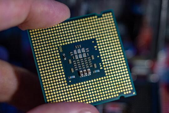Central processing unit held by human fingers showing golden contact pins and electronic components on green circuit board