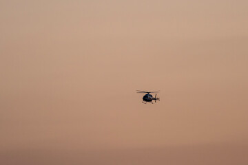 Fototapeta premium Sunset Helicopter Flying Through the Evening Sky. Helicopter Silhouette Against a Colorful Sunset Sky. Golden Sunset Sky Featuring a Flying Helicopter.