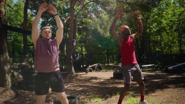 Whip pan shot of Caucasian young adult man and African American young adult man performing jumping jacks at outdoor gym. Clip is ideal for fitness apps, health campaigns, and sports marketing