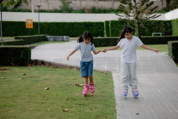 Fototapeta premium Two young girl kids smiling and holding hands learning roller skating together on path in park during outdoor childhood lifestyle activity and leisure time.