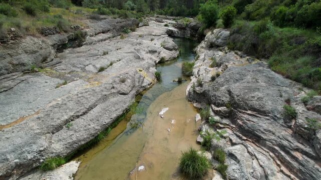 Forward reveal aerial shot of Charca del Molino (natural limestone pool) on sunny day. Arnes, Tarragona, Spain.