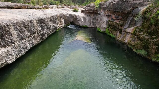 Aerial footage of Charca del Molino (natural limestone pool) on sunny day. Arnes, Tarragona, Spain.