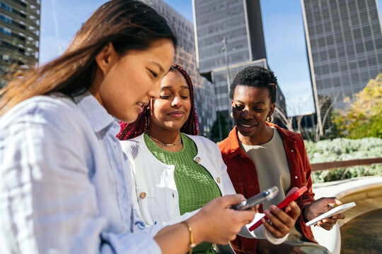 Female friend group using smartphone outdoors in city