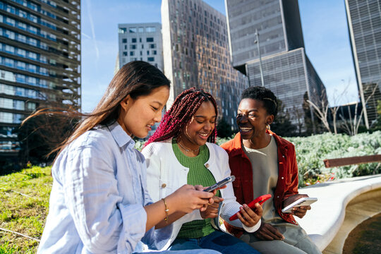 Female friends using smartphone together in city park