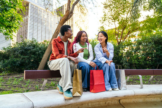 Female friend chatting with shopping bag on city bench