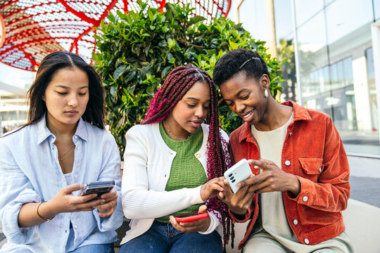 Female friends sharing smartphone and chatting outdoors