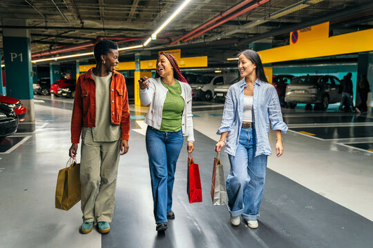 Three female friends walking in parking garage with bags