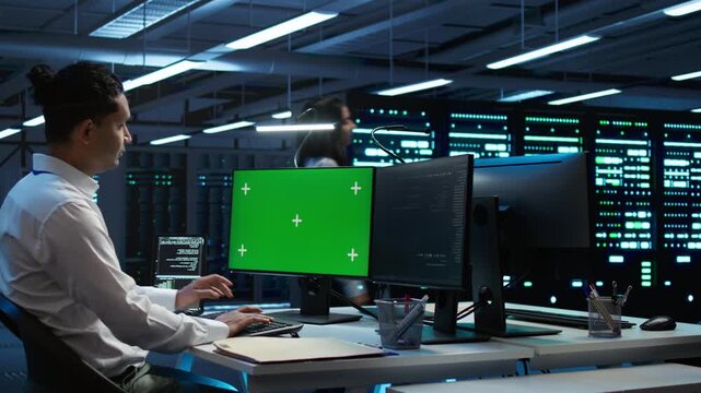 Programmer monitors cybersecurity risks in a server room with a chroma key computer monitor, supporting network security, data protection and screen replacement during secure technical operations