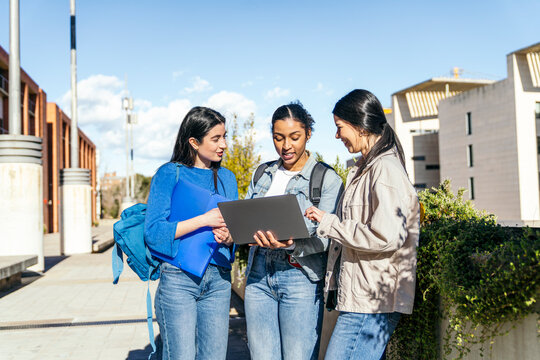 University students using laptop together on campus walkway