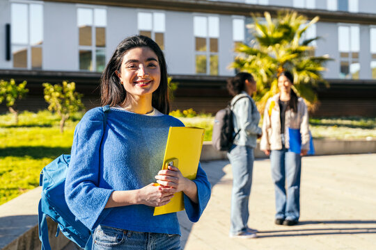 Smiling university student with notebook on sunny campus