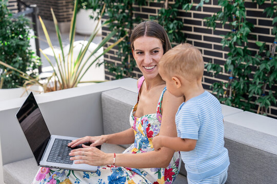 Mother working on laptop outdoors while her son watches