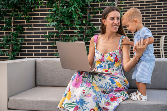 Mother and son using laptop together on outdoor sofa