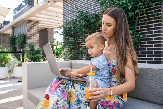 Mother and son using laptop together on outdoor patio sofa