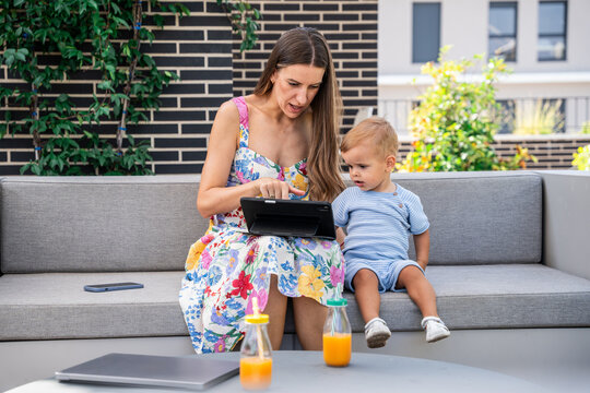 Mother and toddler son using tablet on outdoor sofa