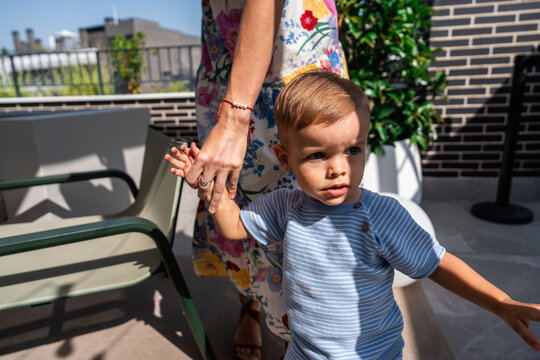 Mother holding toddler sons hand on sunny rooftop terrace