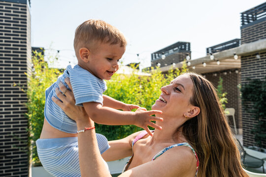 Mother lifting son outdoors in sunny backyard garden