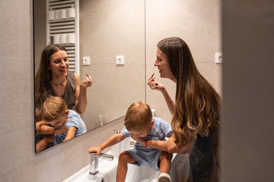 Busy mother applying makeup while toddler plays in bathroom