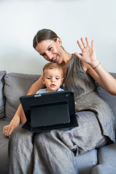 Mother and son video calling on tablet while waving hello