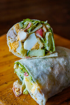 Close up of a fresh chicken salad wrap filled with egg, lettuce, cucumber and tomato on rustic wooden board. Healthy high protein meal, clean eating concept, natural light food photography.