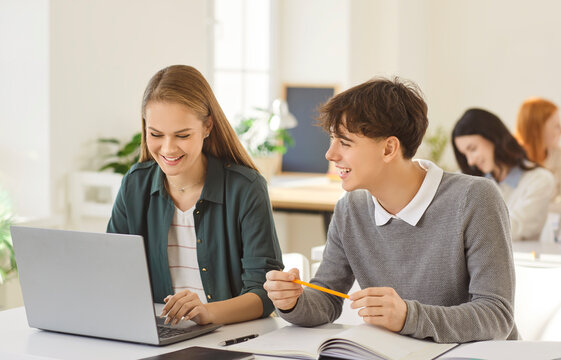Cheerful students learning together during lesson in high school classroom, using laptop for education and knowledge in a supportive setting with focus on collaboration and growth daily.