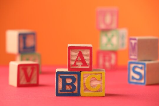 Wooden cubes with letters on pink table against orange background, closeup