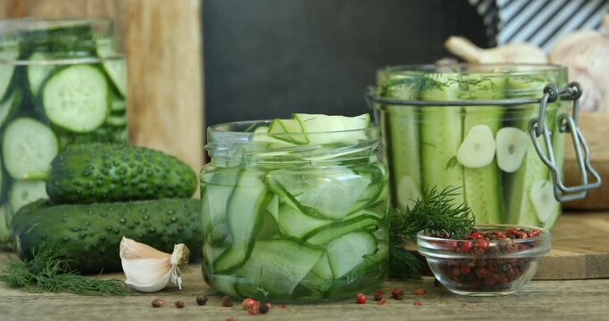 Woman putting lid onto glass jar with pickled cucumbers at wooden table, closeup