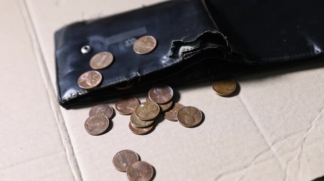 Poor financial situation. Coins falling onto old wallet on cardboard, closeup