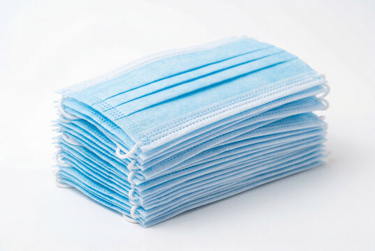 Neat stack of light blue disposable surgical face masks on a white background