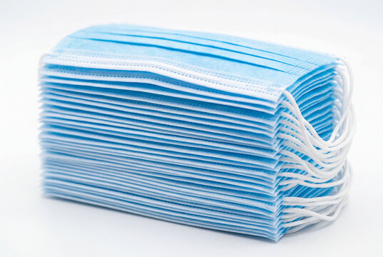 Thick stack of light blue surgical face masks on a white surface