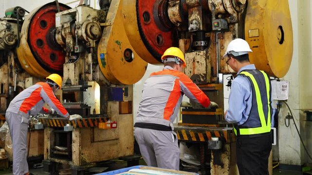 Team of workers collaborating in a manufacturing environment equipped with heavy machinery and essential safety gear