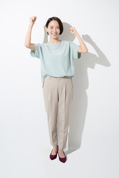 白背景で笑顔でガッツポーズをする日本人女性 成功・達成・応援を表現する働く女性の全身イメージ