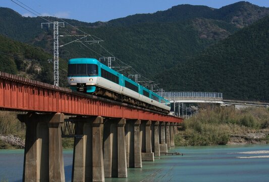 ​澄み切った青空と山々を背に川の鉄橋を渡る特急電車