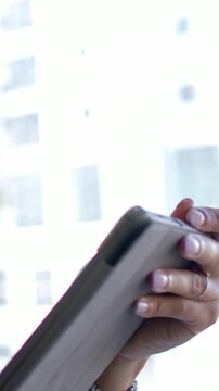 Vertical video: Holding hands, tapping and adjusting tablet case by bright window, cuff, copy space