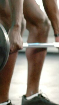 Vertical video: Hands reaching, man grasping barbell and lifting at gym in shorts with spotter