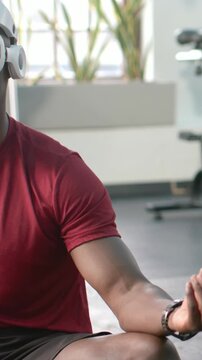 Vertical video: Cooling down man holding calm pose on gym mat with red tee, headphones, copy space
