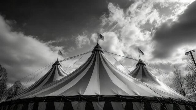 A traditional circus tent with striped top under a dramatic sky.
