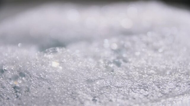 Abstract macro shot of white soapy bubbles forming on water surface with dynamic movement.