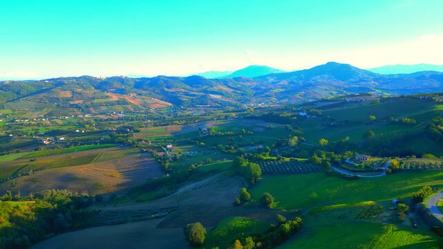 Fresh aerial truck left pan right shot from Monte Rinaldo, sharp and detailed views of the countryside adorning the town, imbued with spiritual sunlight, sunflares, hillscapes and Sibillini mountains