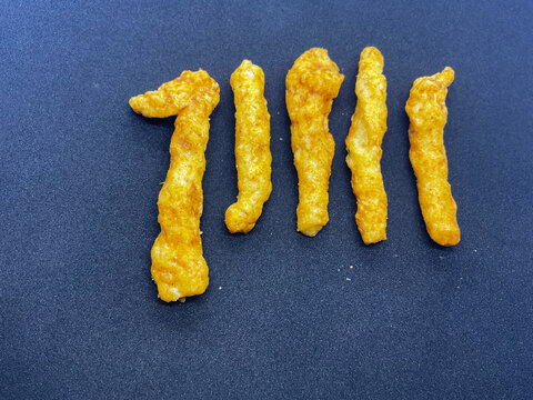 Spicy Indian Kurkure Corn Puff Snacks namkeen sticks arranged neatly in a row on a clean black backdrop. Perfect for food branding, commercial packaging, snack advertising, and junk food concepts.