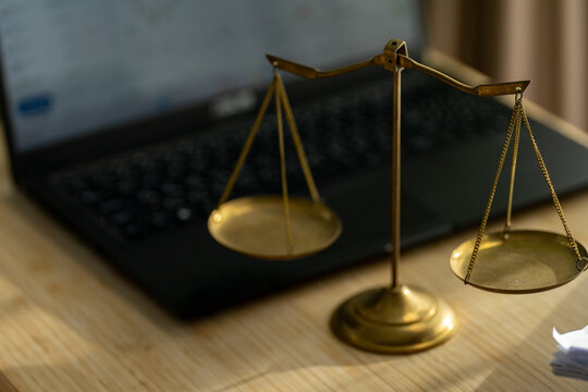Golden scales rest beside a laptop on wooden surface. Soft focus highlights metallic balance and digital presence. Symbolic scene merges law, technology, and modern decision-making