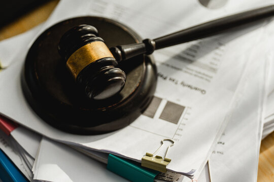 Wooden gavel rests on documents. Paperwork piles beneath a judge's hammer. Clips and pens lie nearby, ready for use. Legal matters feel urgent and serious. Ideal for law, finance, or courtroom themes