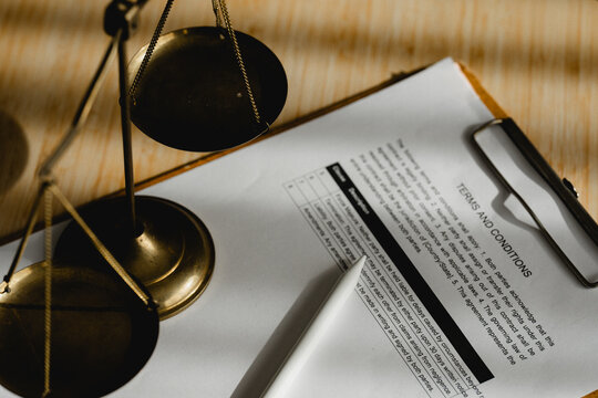 Golden scales rest beside a legal document. Paper holds fine print and clear headings. Clipboard holds the document steady. Wooden surface shows soft, natural grain