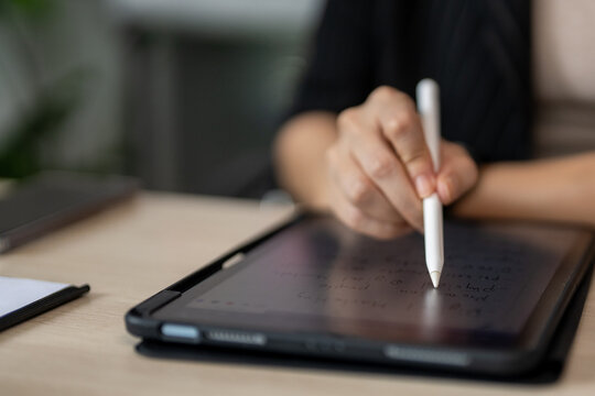 Hand holds stylus above tablet screen. Fingers poised to write, focused, calm. Light wood desk, soft blurred background. Ideal for digital creativity, education, or work. No animals or plants present