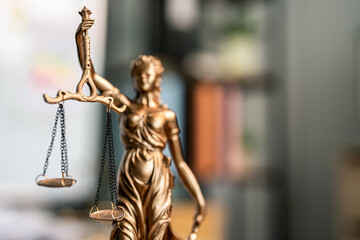 Golden statue holds scales, symbolizing justice. Blurred background adds depth to the scene. Statue stands solemn, representing fairness and balance. Ideal for legal, court, or ethical topics © WARAPHON